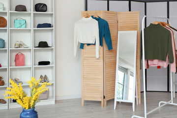 Interior of clothing shop with folding screen, mirror and shelf unit