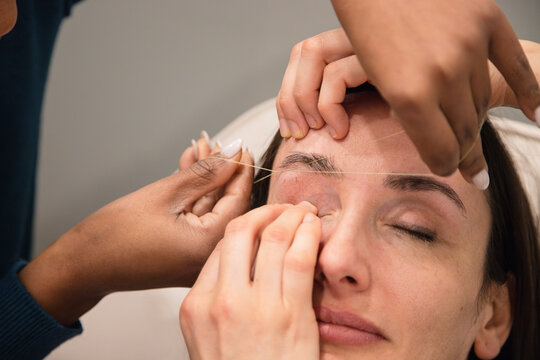 Caucasian woman removing hair from eyebrows with thread technique done by eyebrow stylist. Threading. Process Steps. Close up	