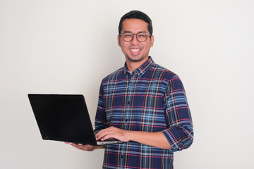 Adult Asian man smiling at the camera while holding a laptop