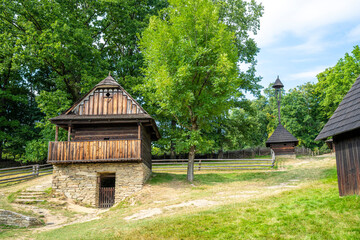 Wooden church with old wooden wallachia houses in old village with green meadow and trees. Roznov pod Radhostem. Czech Republic.