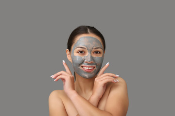 Young woman with clay mask on her face against grey background