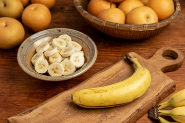 Preparing sweet fruit snacks. Peeled sliced banana in a bowl, a whole banana on a cutting board.  Homegrown, ripe chojuro pears behind.