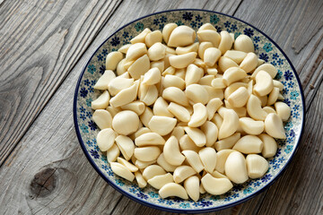 A heap of peeled garlic cloves on a plate. Naturally aged wooden table.