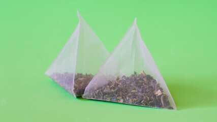 Two pyramid tea bags with green tea, mint leaves and fruit flavourings lie on a bright green...