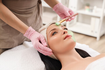 Young woman receiving facial mask in beauty salon, closeup