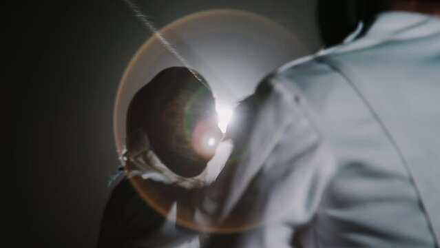 Rear slowmo of unrecognizable fencer fighting with rapier with swordswoman in epee mask during competition in dark foggy room