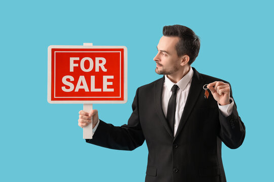 Portrait of male real estate agent with FOR SALE sign and keys on blue background