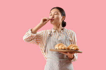 Female Asian baker with fresh croissants on pink background