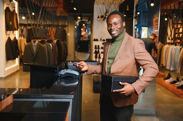 Happy african shopper holding boxes of new clothes or shoes and paying with phone