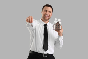 Male realtor with keys and house model on light background