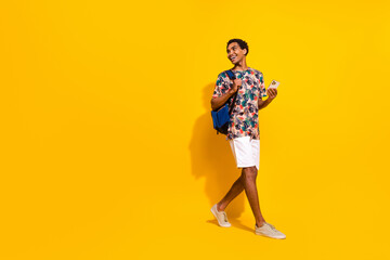 Fototapeta na wymiar Full length photo of positive man wearing casual summer outfit bring phone and backpack look copyspace isolated on yellow color background