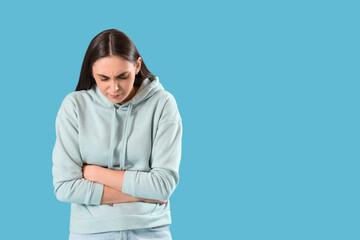 Young woman suffering from bellyache on blue background