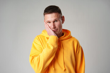 Portrait of young man in yellow hoodie with face palm gesture on gray background
