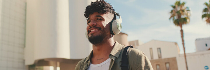 Young man with beard in an olive-colored shirt listens to music on headphones, Panorama