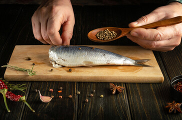The cook is preparing herring with spices and coriander on the kitchen table for a delicious dinner. Working environment on the kitchen table with spices and pepper.