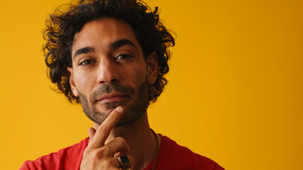 Close-up of a dreamy man with curly hair wearing red T-shirt look at camera, isolated on yellow...