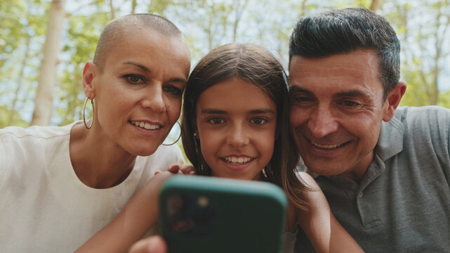 Close up, happy family, mom dad and daughter, spending time together, using smart phone looking at pictures and videos sitting in park bench