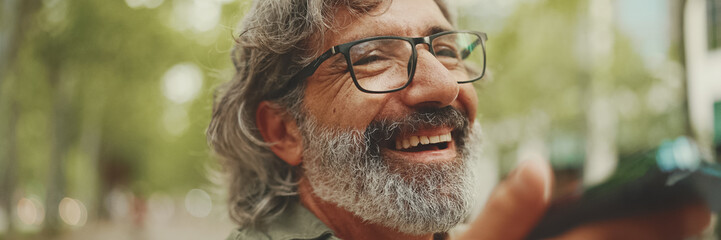 Clouse-up, Panorama of smiling middle-aged man with gray hair and beard sits on bench and uses...