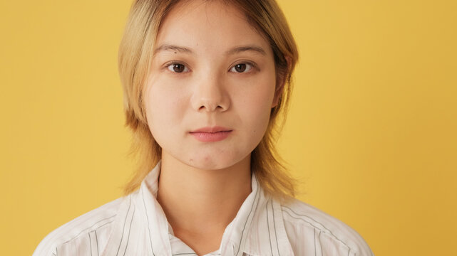 Portrait of young woman looking at camera, isolated on yellow background in studio