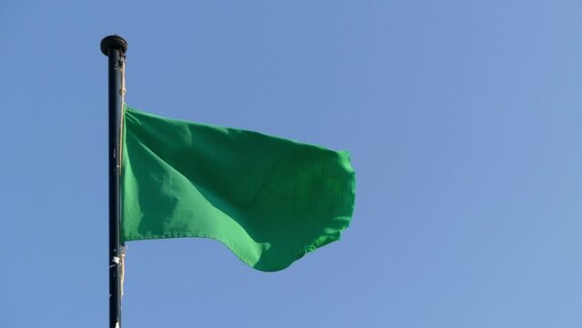 Green flag moves on wind against blue day sky.