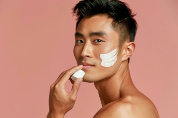 Side view of a confident shirtless man of Asian descent applying a hydrating facial cream with a serene expression, emphasizing his skin care routine. 
