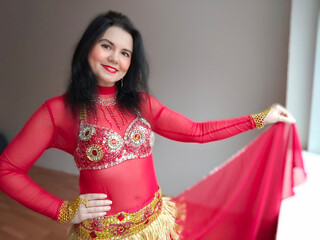 A dancer in a red suit is dancing an oriental dance on a white background. A professional dancer...