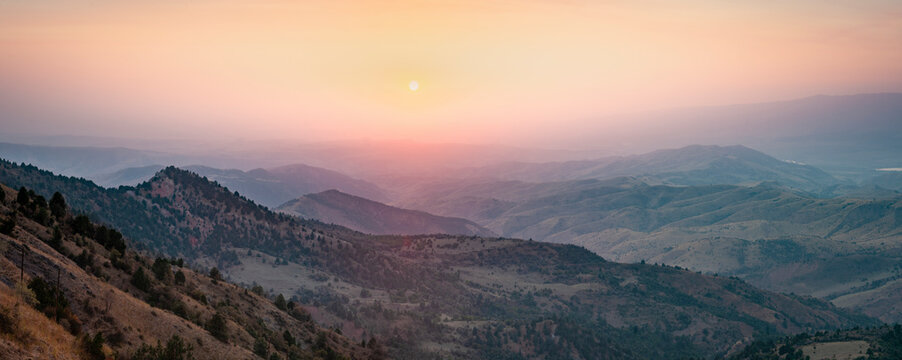 Aerial view of Uzbekistan's vast and beautiful landscape at sunset, overlooking the rolling hills and rugged terrain, with a serene and tranquil atmosphere.