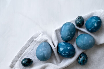 Blue dyed Easter eggs on crumpled neutral beige linen tablecloth and white marble table background,...