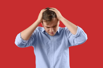 Young man suffering from headache on red background