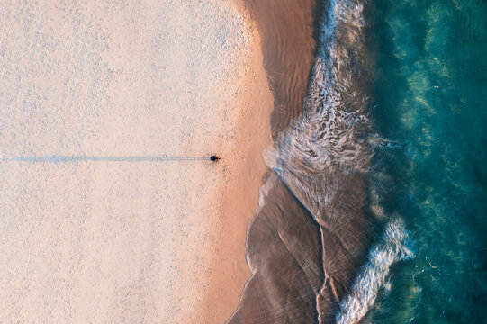 Aerial view of a photographer on the beach from above with blue ocean water and long exposure effect on the waves, Port Noarlunga, South Australia, Australia.