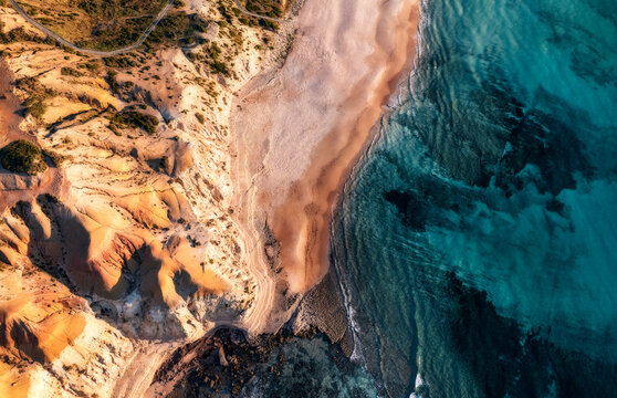 Aerial view of limestone cliffs with a sunset hue and blue coastal water from above, Port Willunga, South Australia, Australia.