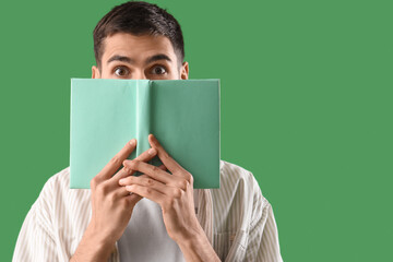 Shocked young man with book on green background, closeup