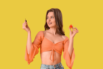 Young woman with bottle of nail polish on yellow background