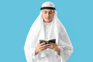 Young Muslim man with Koran on blue background. Ramadan celebration