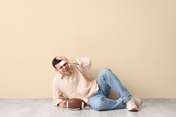 Obraz premium Young man with brain concussion and rugby ball lying near beige wall