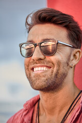 Vertical portrait of an attractive adult man smiling as the evening sun reflects on his sunglasses. Summer holidays on the Mediteranean coast.
