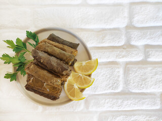 Delicious traditional oriental dolma made of grape leaves stuffed with rice on a plate with parsley and lemon slices