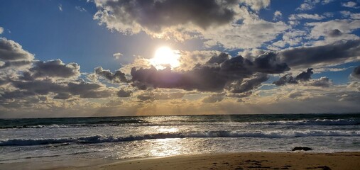 Naklejka na ściany i meble Sunset at the beach with the sun peeking through