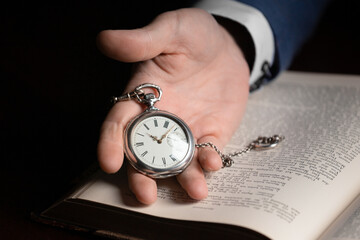 A hand holds a vintage pocket watch on the background of an old book.