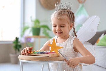 Cute little girl dressed as fairy playing with xylophone at home