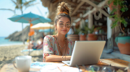 young latina woman working on a laptop in a restaurant at the beach, wearing a floral dress and has her hair in a bun. - obrazy, fototapety, plakaty