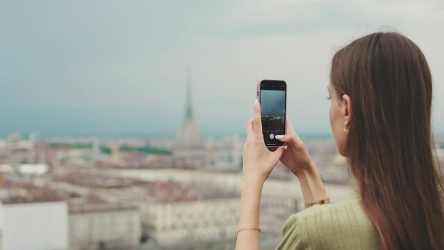 Young woman on the observation deck of the city takes photos and videos on her mobile phone