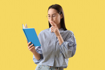 Thoughtful young woman reading book on yellow background