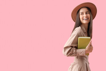 Young woman in hat with book on pink background