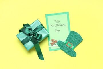 Paper leprechaun hat with gift box and festive postcard on yellow background. St. Patrick's Day...