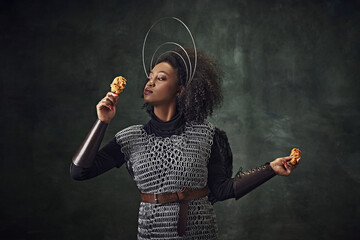Young African woman, medieval warrior in chainmail armor holding fried chicken against vintage...