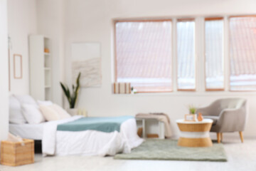 Blurred view of light bedroom with big bed, armchair and window