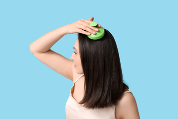 Beautiful young woman using hair scalp massager on blue background