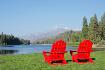 A two red wooden armchairs in front a beautiful view of a lake and a mountain