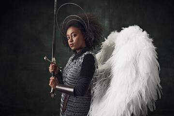 Young African woman, medieval warrior with angel wings, halo above head and chainmail holding sword...